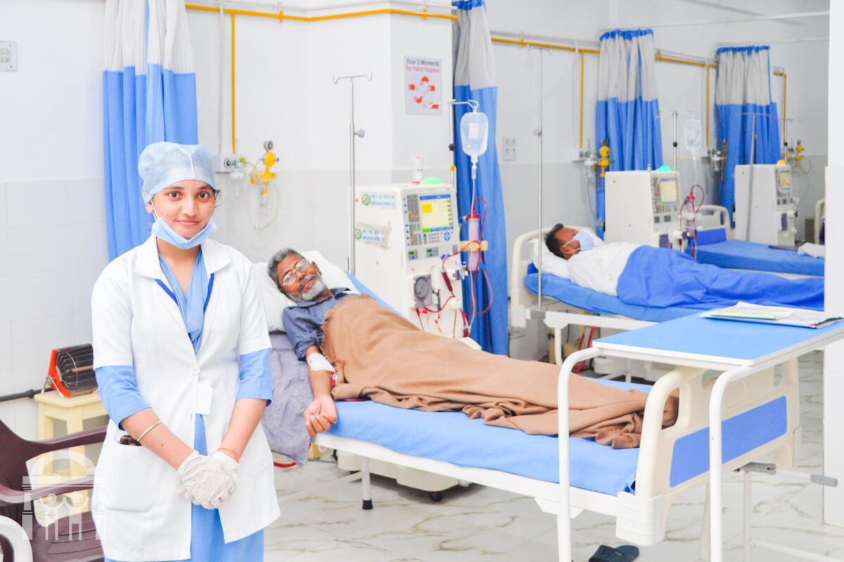 Nurse in front of dialysis unit with patients on beds in the background at Guru Nanak Mission Hospital Dhahan Kaleran near Banga in Punjab
